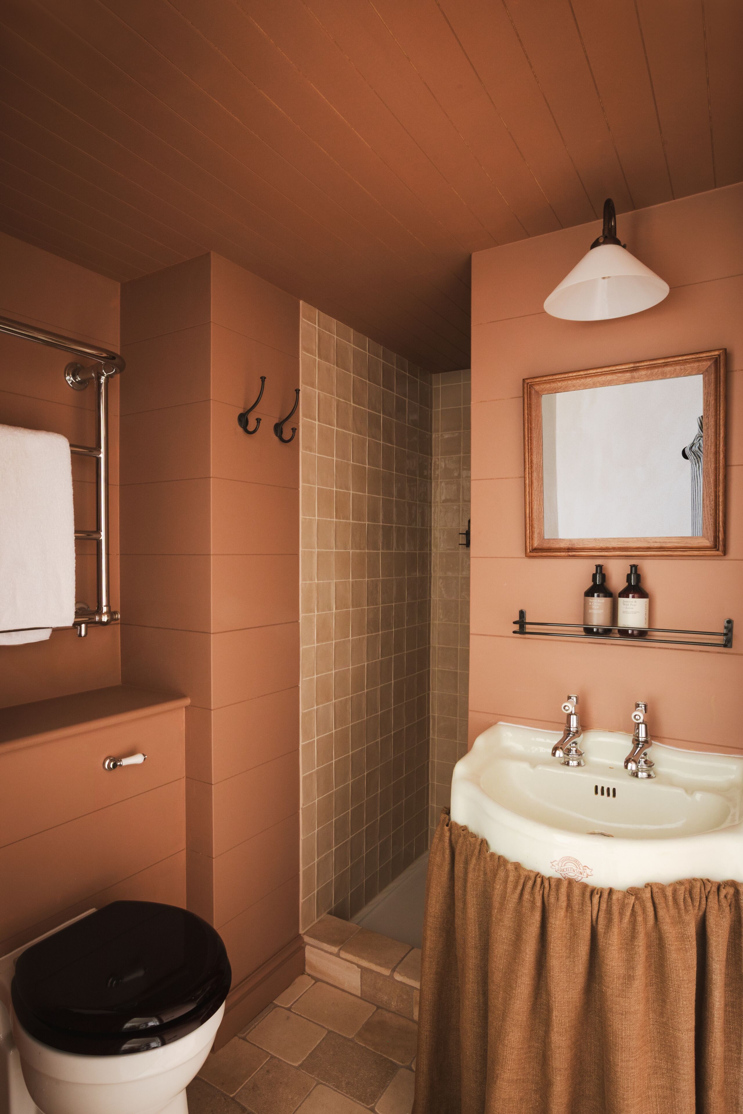 A bathroom with a toilet, sink, mirror, shower, and towel rack.
