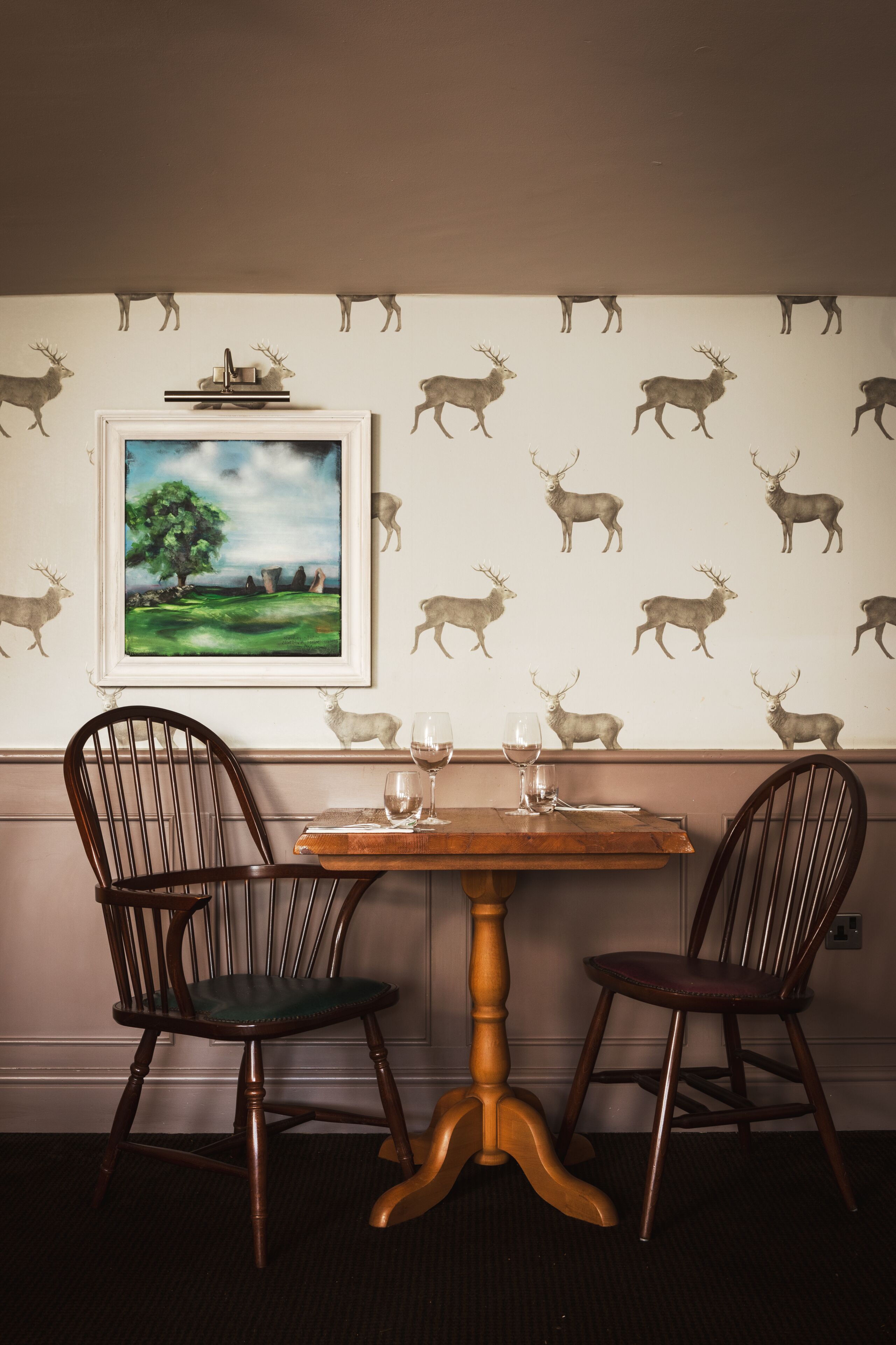 A dining area with a table, two chairs, a framed painting, and a wall with deer decals.