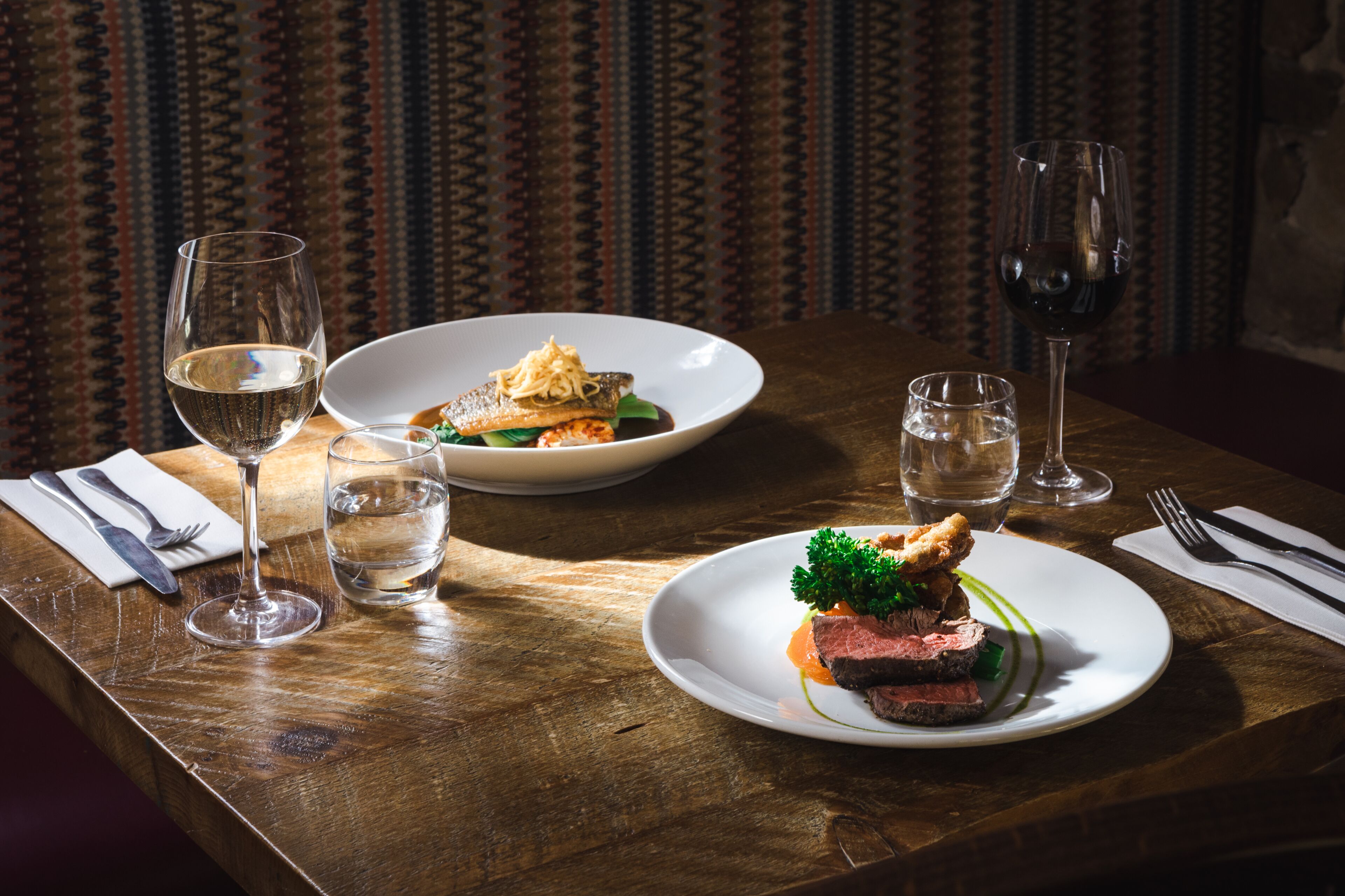 A dining table with plates of food, glasses of water, and wine glasses.