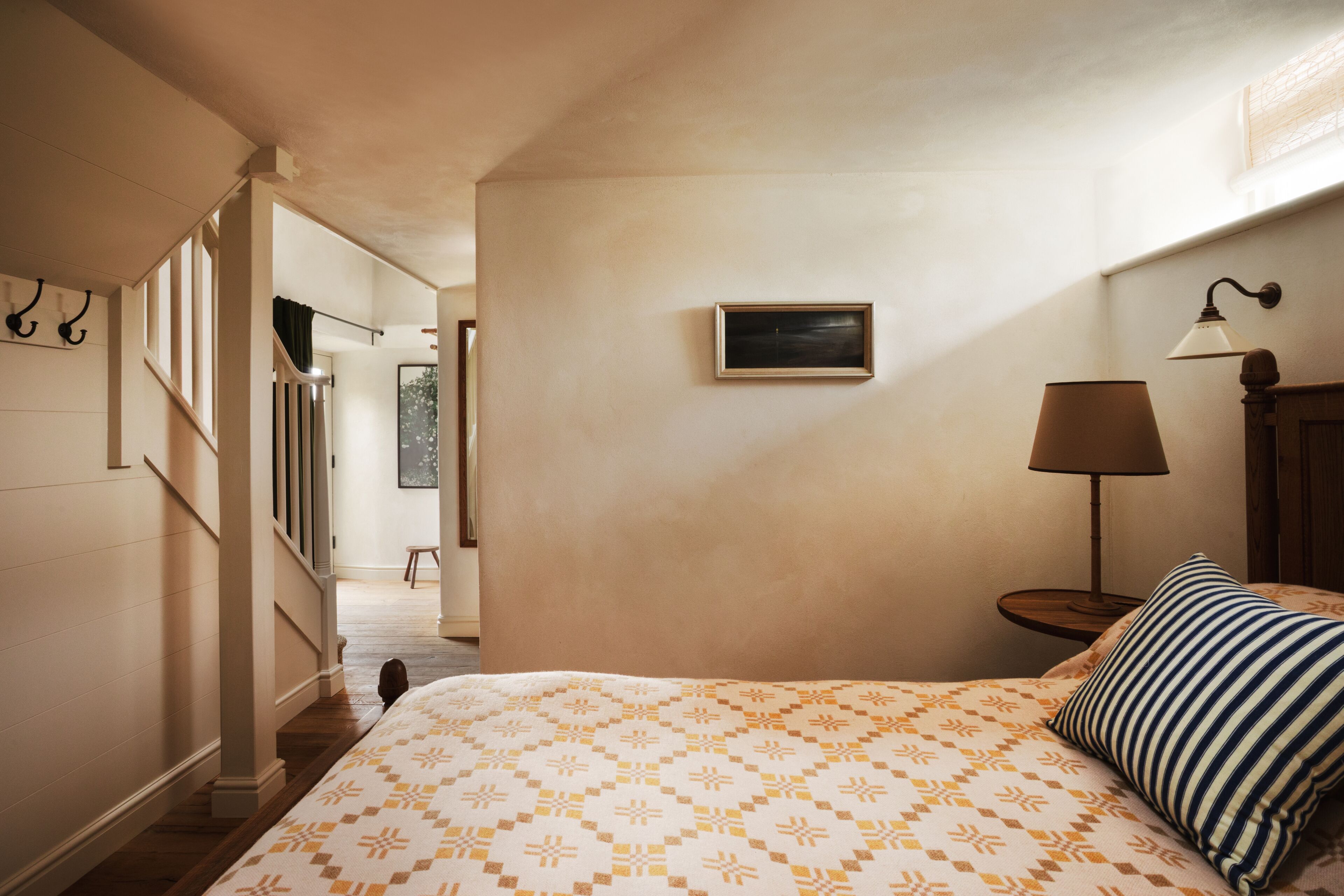 A bedroom with a bed, a nightstand, a lamp, a picture on the wall, and a staircase leading to another room.