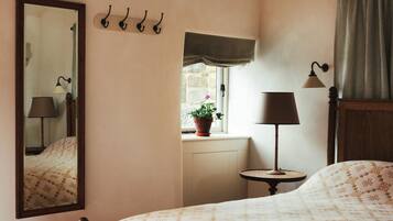 Un dormitorio con cama de madera, espejo, mesita de noche con lámpara, ventana con vista al exterior y un aplique en la pared.