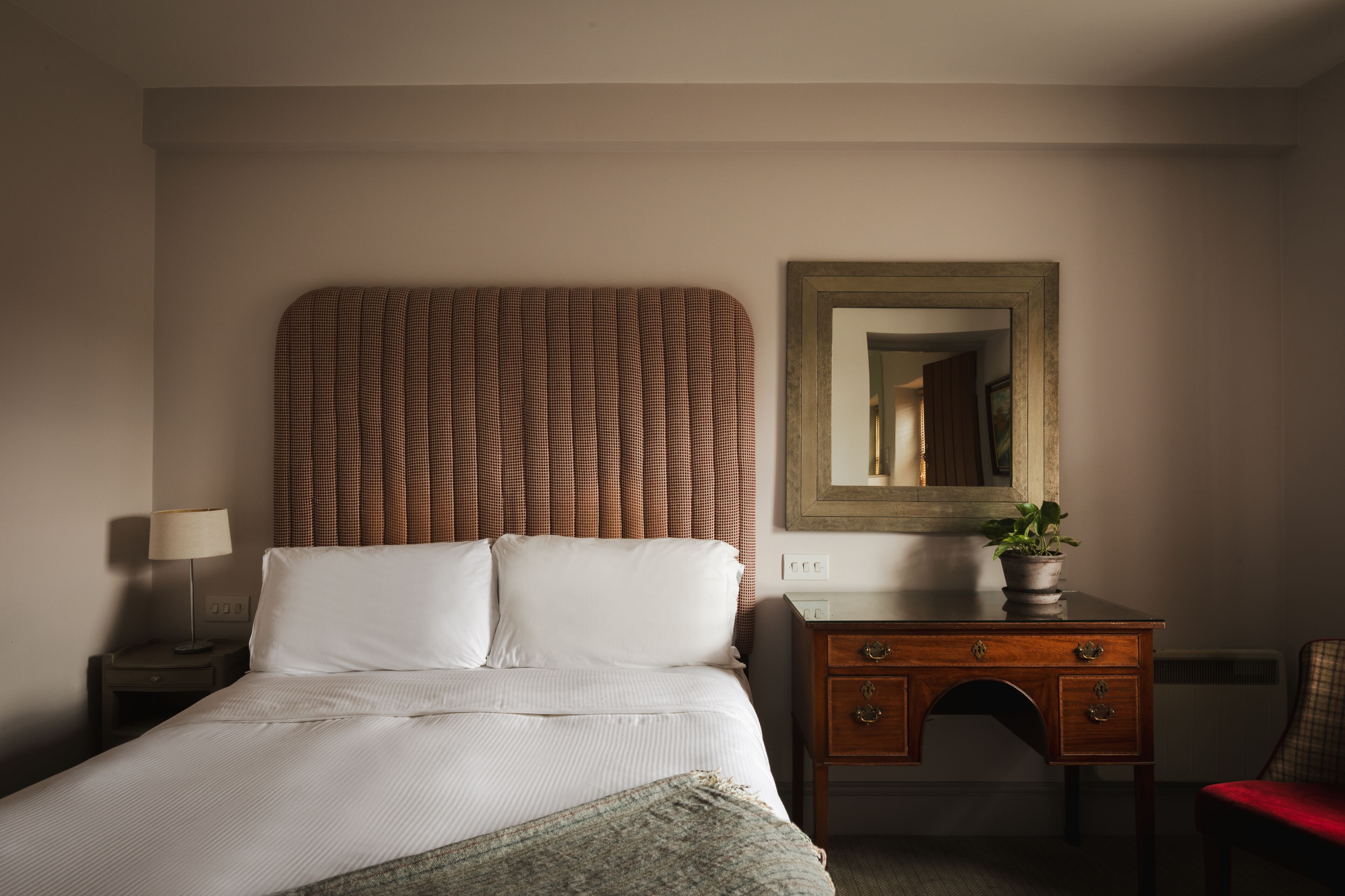 A hotel room with a bed, a nightstand, a dresser, a mirror, and a potted plant.