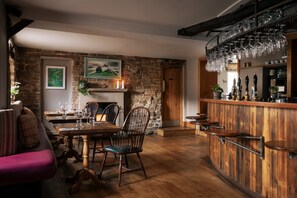 A rustic interior with a wooden dining table, chairs, a bar area with a wine rack, and a fireplace. - The Pilsley Inn (Bakewell)