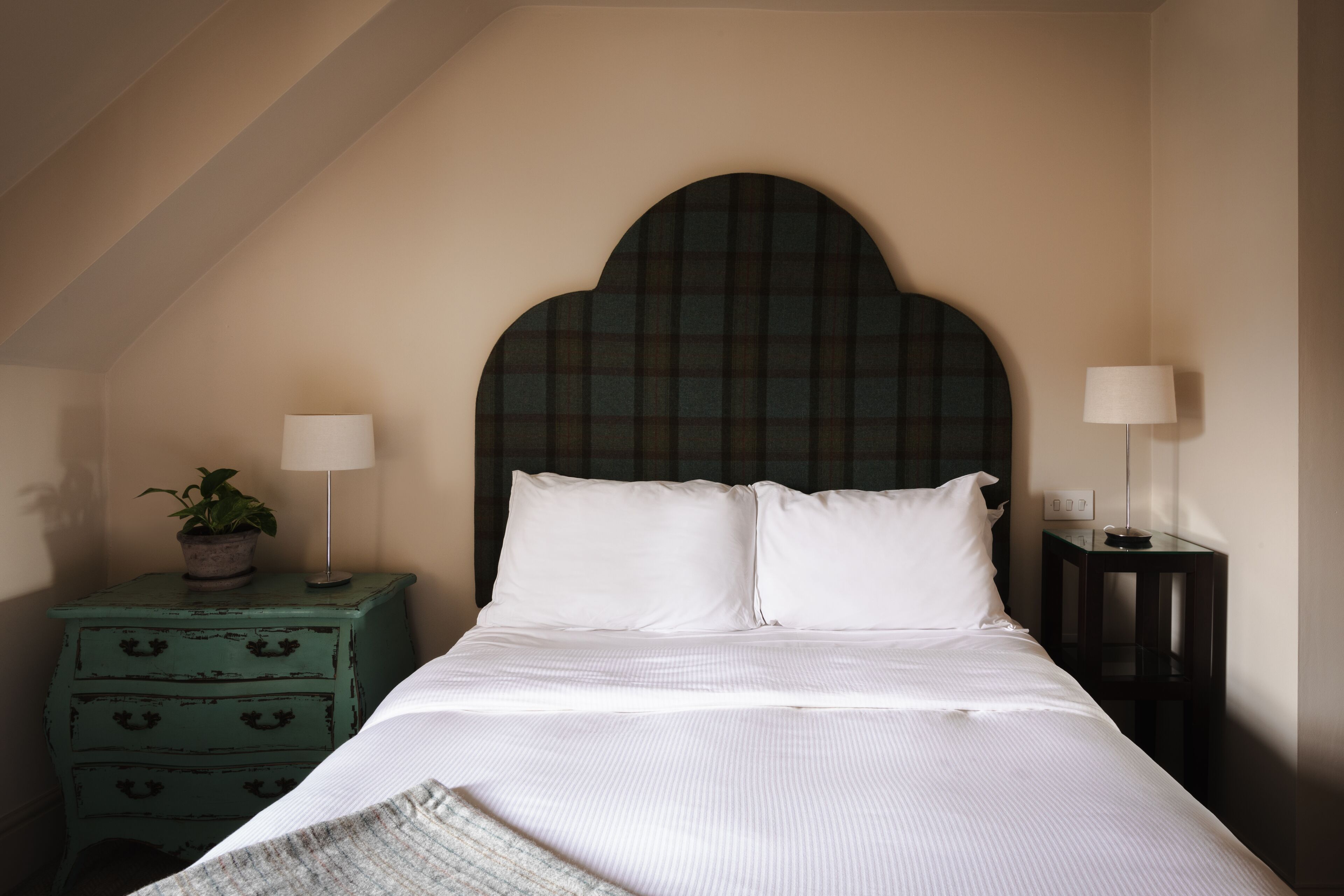 A bedroom with a bed, two bedside tables, a nightstand, a lamp, and a potted plant.