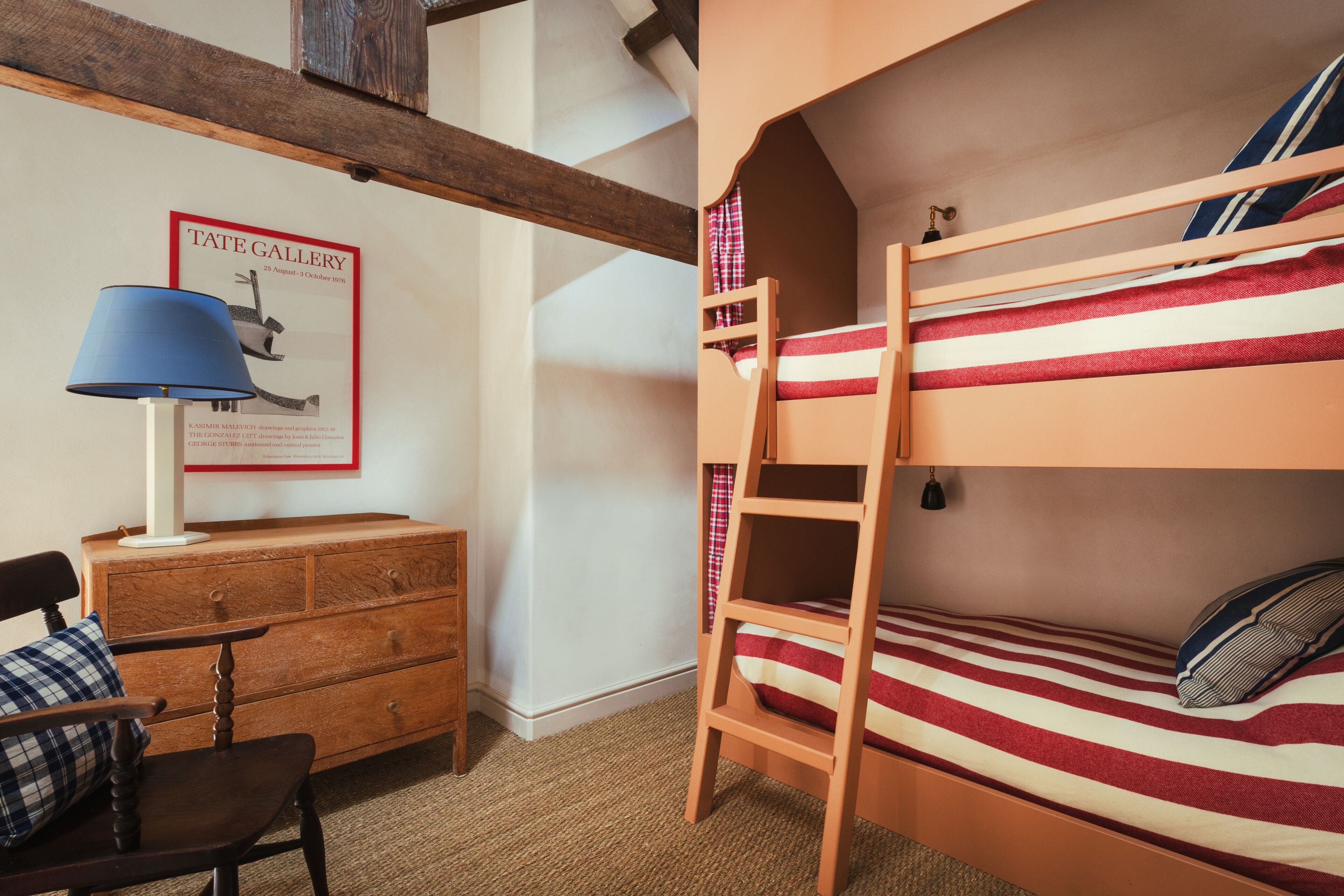 A bunk bed with a ladder, a wooden dresser, a chair, and a lamp.