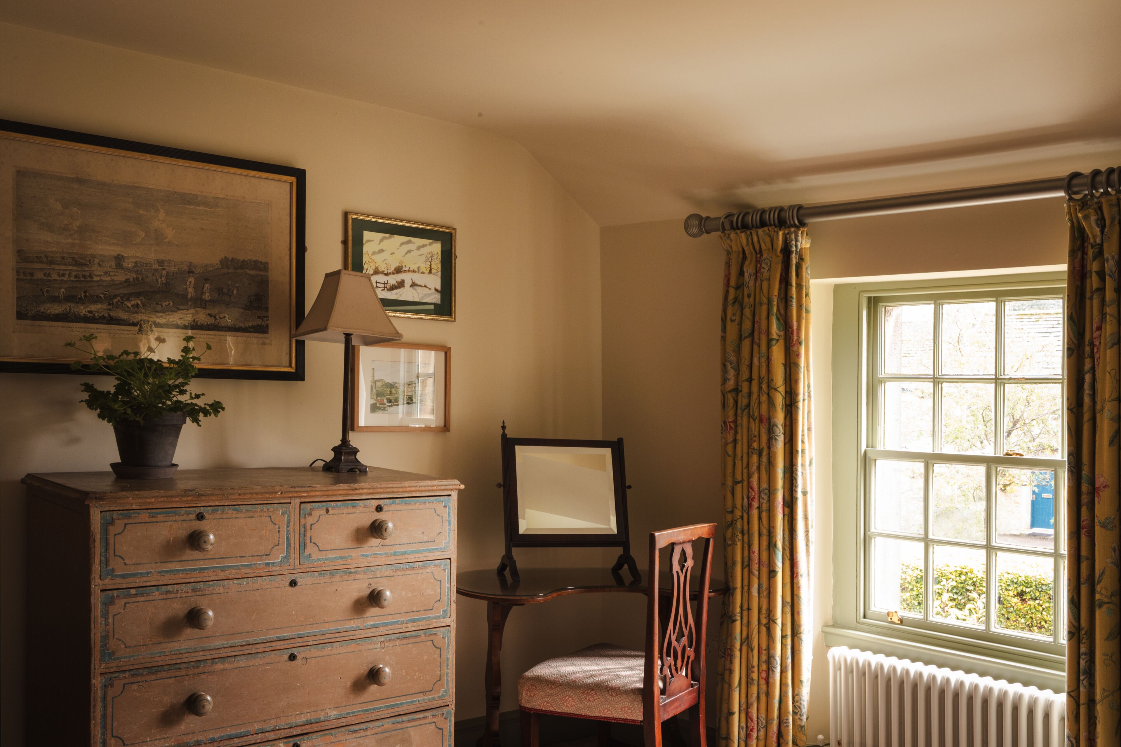 A room with a wooden dresser, a chair, a table, and a window with curtains.