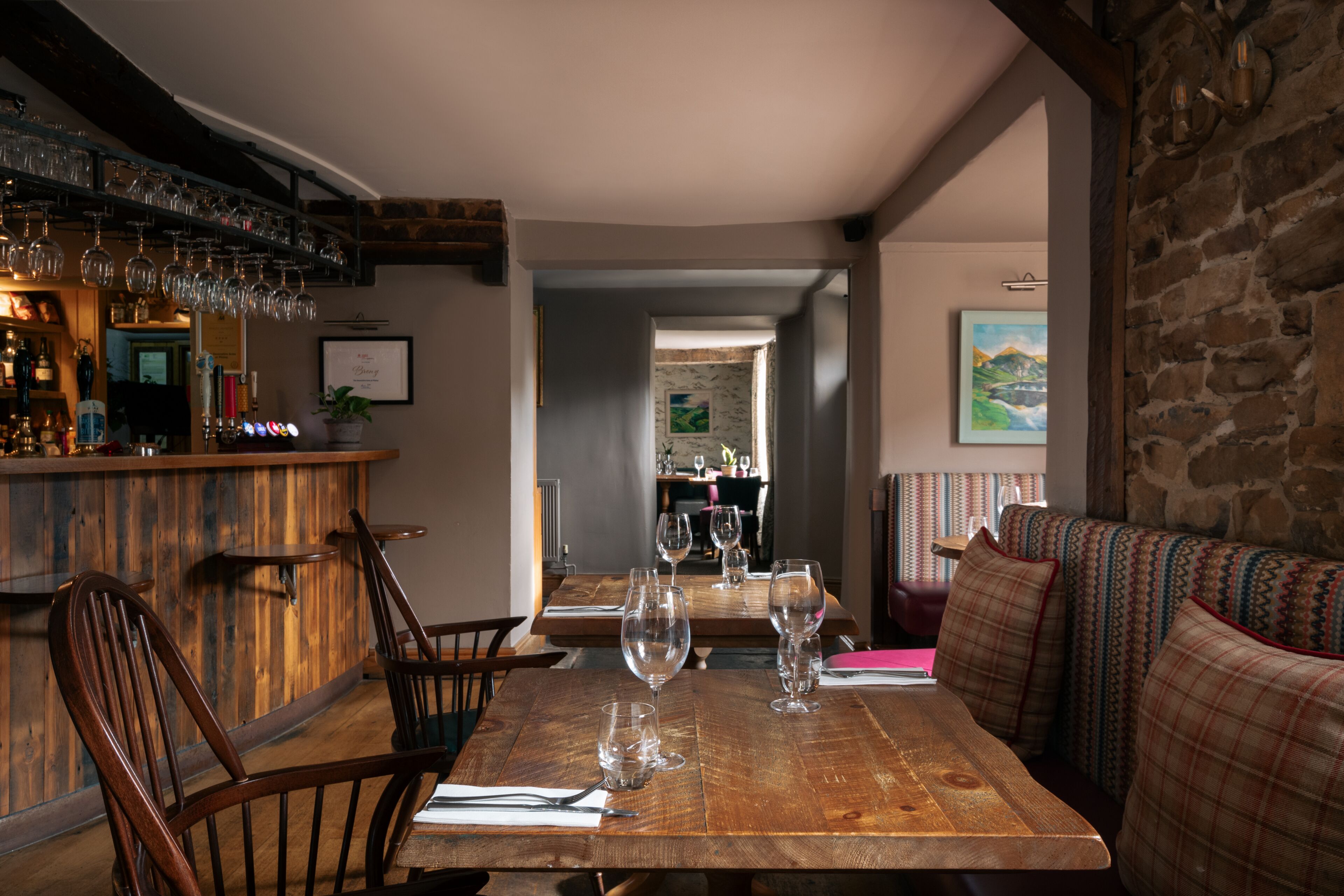 Uma mesa de jantar de madeira com cadeiras, um espaço de bar com copos e vista para a sala de jantar.