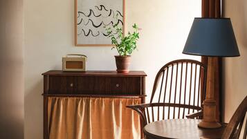 A room with a wooden desk, a chair, a table, a lamp, a framed picture, and a potted plant.