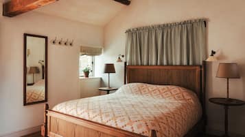 A bedroom with a wooden bed, a mirror, a bedside table with a lamp, and a window with a view of the outside.