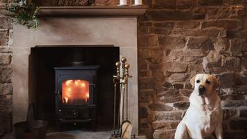A fireplace with a painting above it, a dog sitting beside the fireplace, and a candle holder on the mantel.
