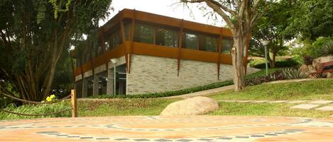 Um edifício moderno com fachada de vidro, rodeado por vegetação exuberante e um caminho de pedra com padrão.