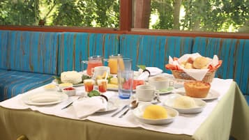 A breakfast table set with various dishes, including eggs, toast, and fruit, in a room with a large window and striped blue and orange seating.