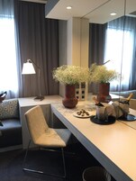 A modern hotel room with a large mirror, a desk with a chair, a vase with flowers, and a bottle of champagne.