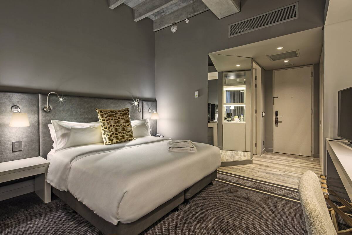 A modern hotel room with a large bed, bedside tables, a desk, and a mirror.