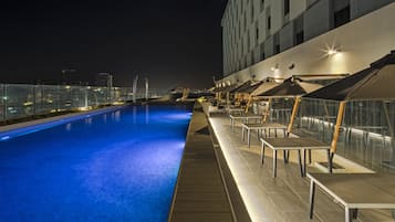 Relax by the pool, surrounded by lounge chairs and umbrellas, with a city view.