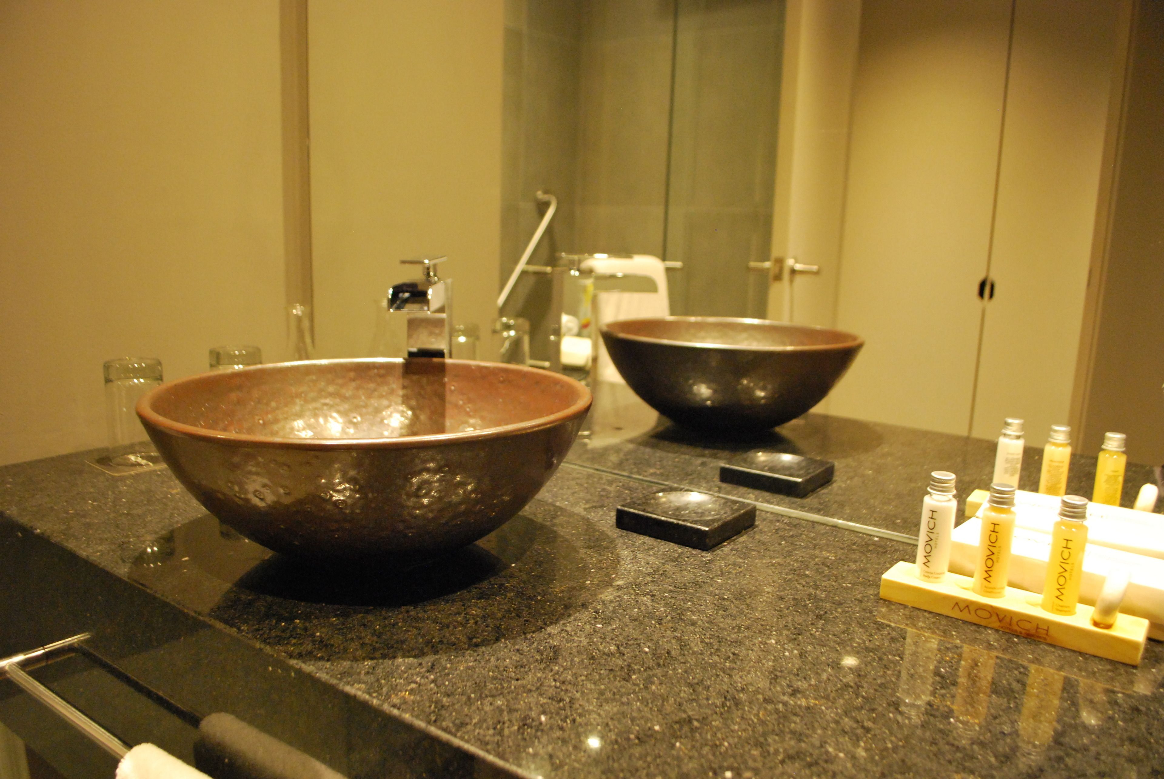 A bathroom with two large ceramic sinks, a mirror, and a soap dispenser stand.