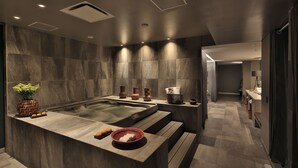 Un baño moderno con una bañera grande, un tocador con espejo y un pequeño rincón de descanso.