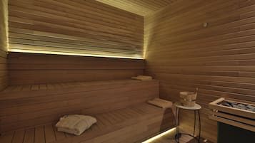 Una sauna de madera con bancos, una mesa pequeña con un balde y un recipiente con piedras.