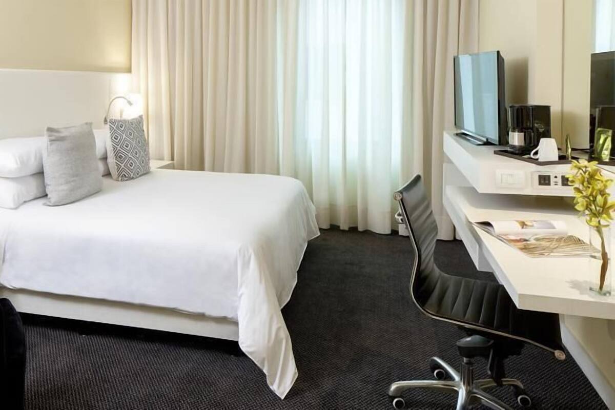 A hotel room with a bed, a desk, a chair, a TV, and a lamp.