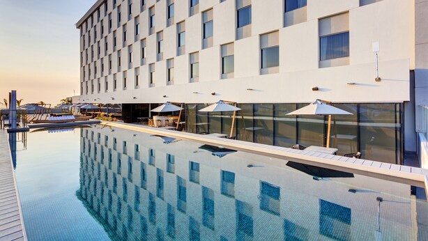 Un hotel moderno con piscina infinita en la azotea, ventanas amplias y zonas de estar al aire libre.