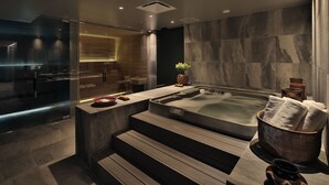 Un moderno espacio de spa con un jacuzzi, escalones de madera y una ducha con paredes de cristal.