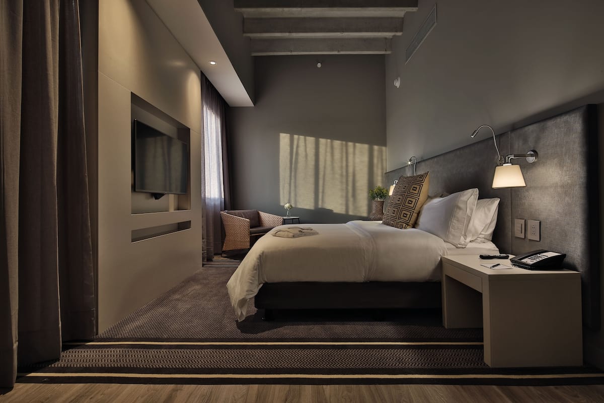 A modern hotel room with a large bed, bedside table, and a flat-screen TV mounted on the wall.