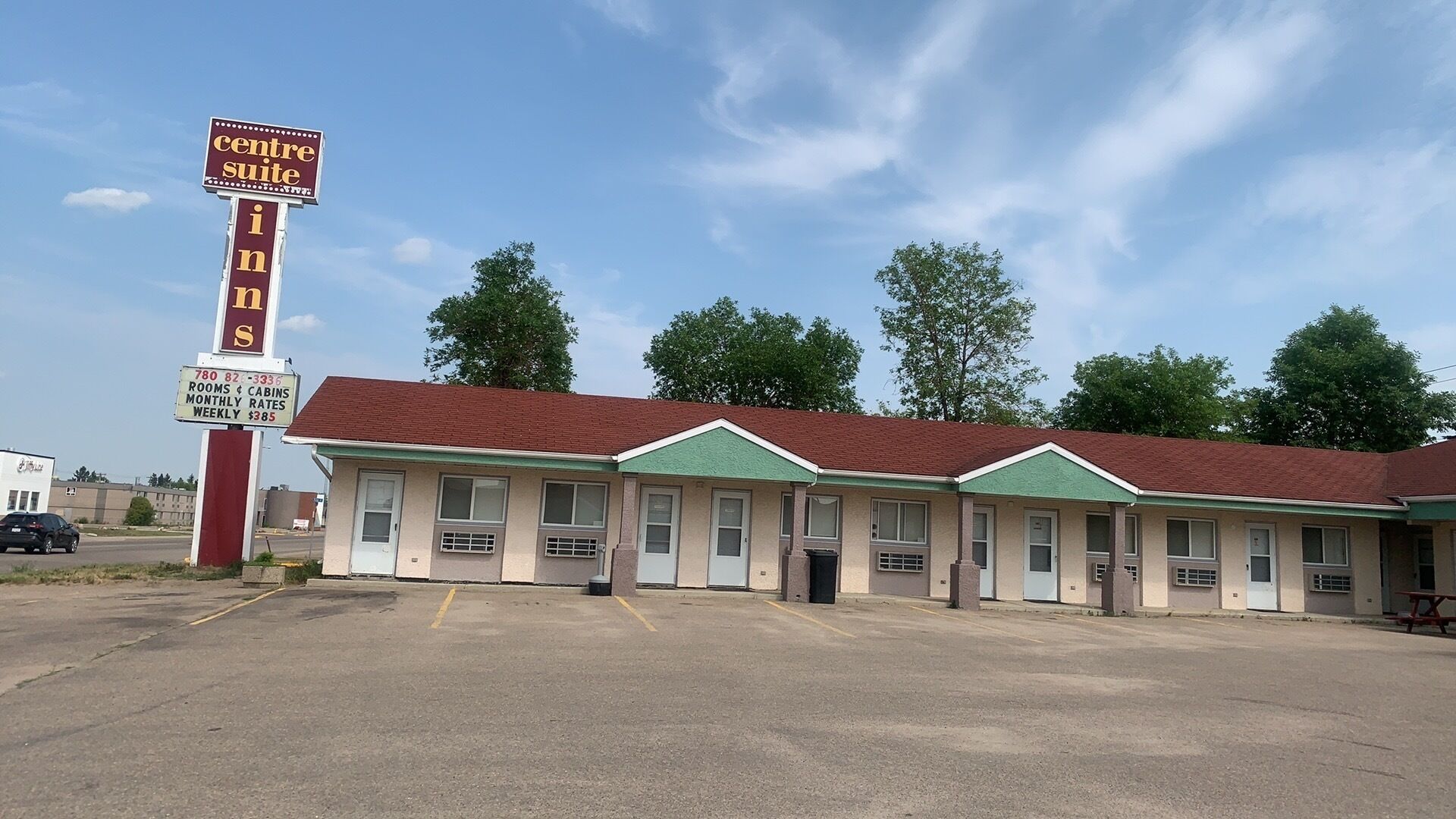 A motel with a central sign advertising rooms and cabins, a parking lot, and a building with a red roof and green trim.