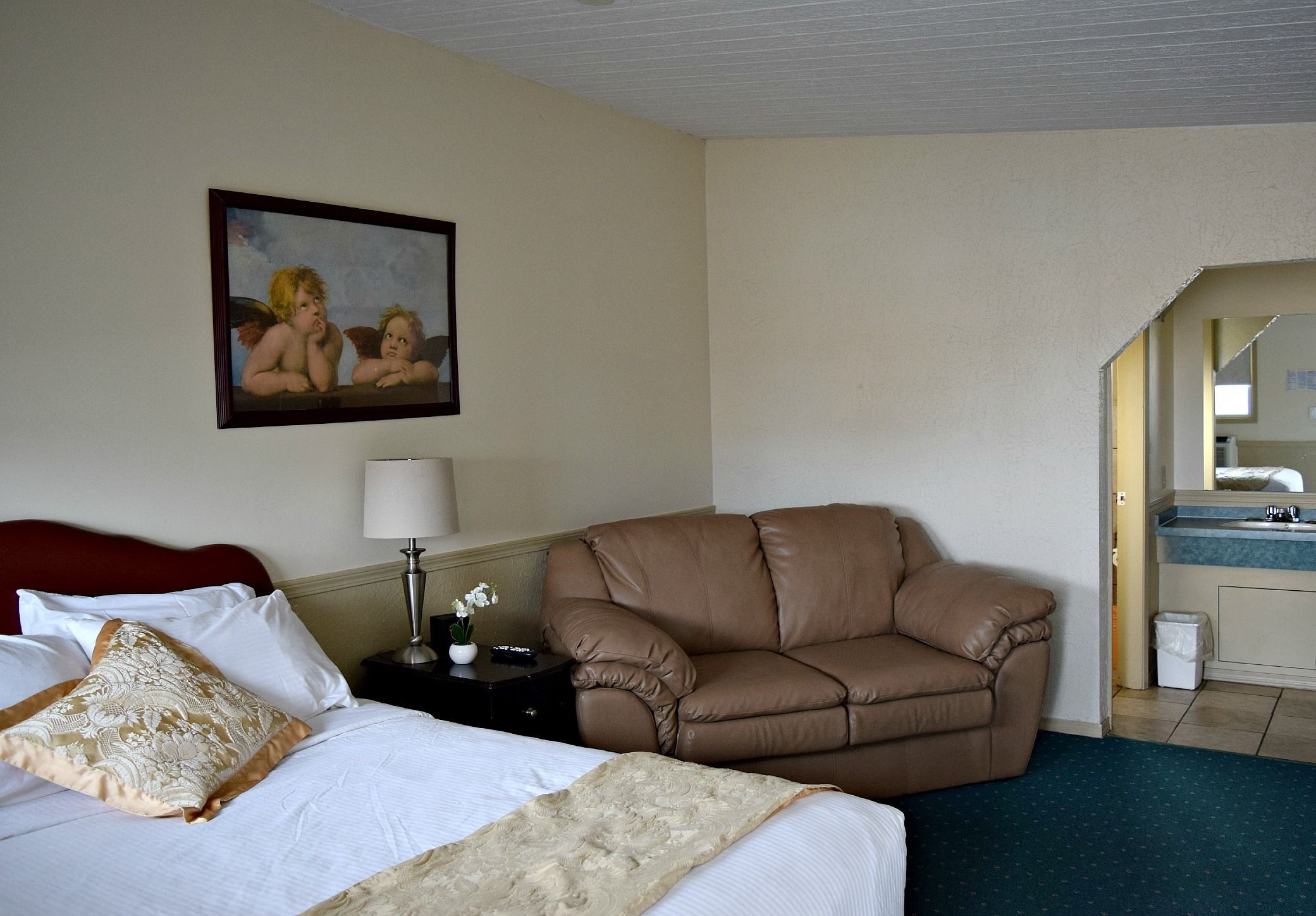 A hotel room with a bed, a brown leather sofa, a nightstand with a lamp, and a painting on the wall.