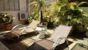 Eine Terrasse mit zwei Korbstühlen, einem Blumentopf und einem kleinen Wasserspiel.