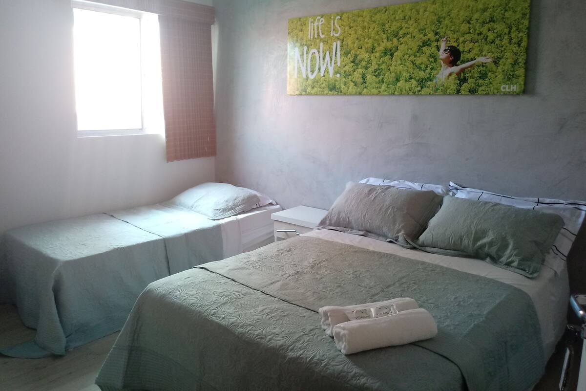 A bedroom with two single beds, a large bed, a window with curtains, and a motivational poster on the wall.