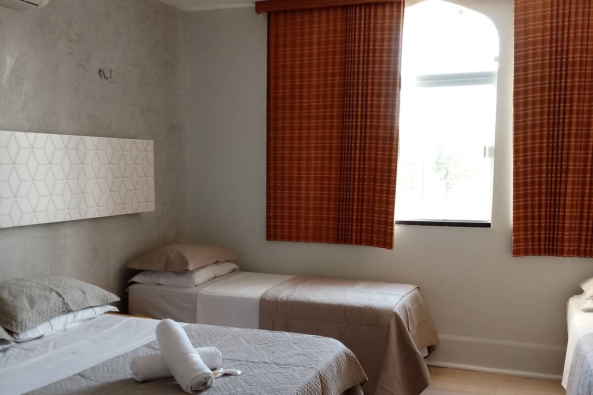 A hotel room with two beds, a window with curtains, a wall-mounted air conditioner, and a small rug.