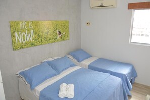 A room with two beds, each with blue bedding and pillows, a wall-mounted air conditioner, and a motivational quote on the wall. - Pousada Hotel Areia da Praia (Fortaleza)