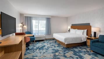 Ein Hotelzimmer mit Bett, Schreibtisch, Stühlen, einem Flachbildfernseher und einem Fenster mit Vorhängen.