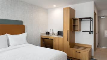 A hotel room with a bed, a wooden desk with a microwave, a sink, and a wardrobe.