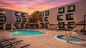 A hotel with a pool, lounge chairs, and a sunset sky.