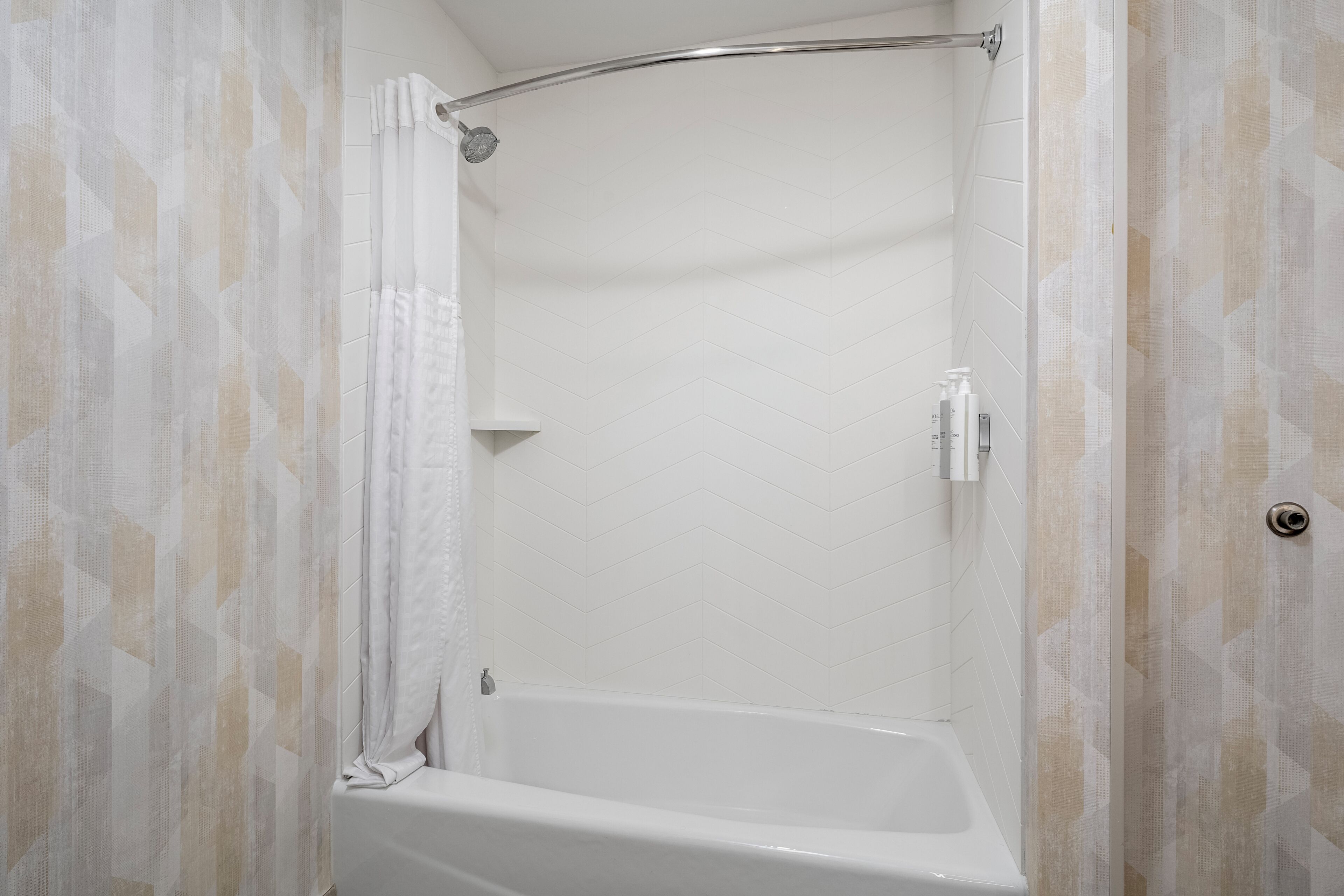 Une douche dotée d’une porte en verre incurvée, une baignoire blanche et un pommeau de douche.