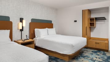 A hotel room with two beds, a bedside table with a phone and remote control, a wall-mounted light, and a wardrobe with a mirror.