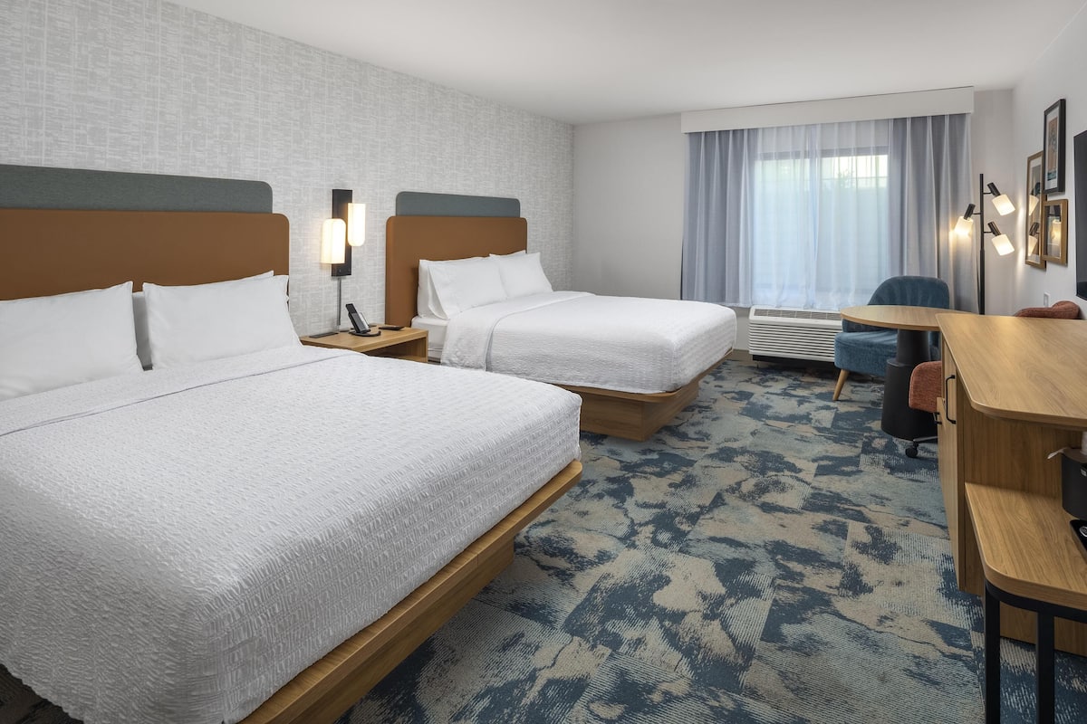 A hotel room with two beds, a desk, a chair, a desk lamp, and a window with curtains.