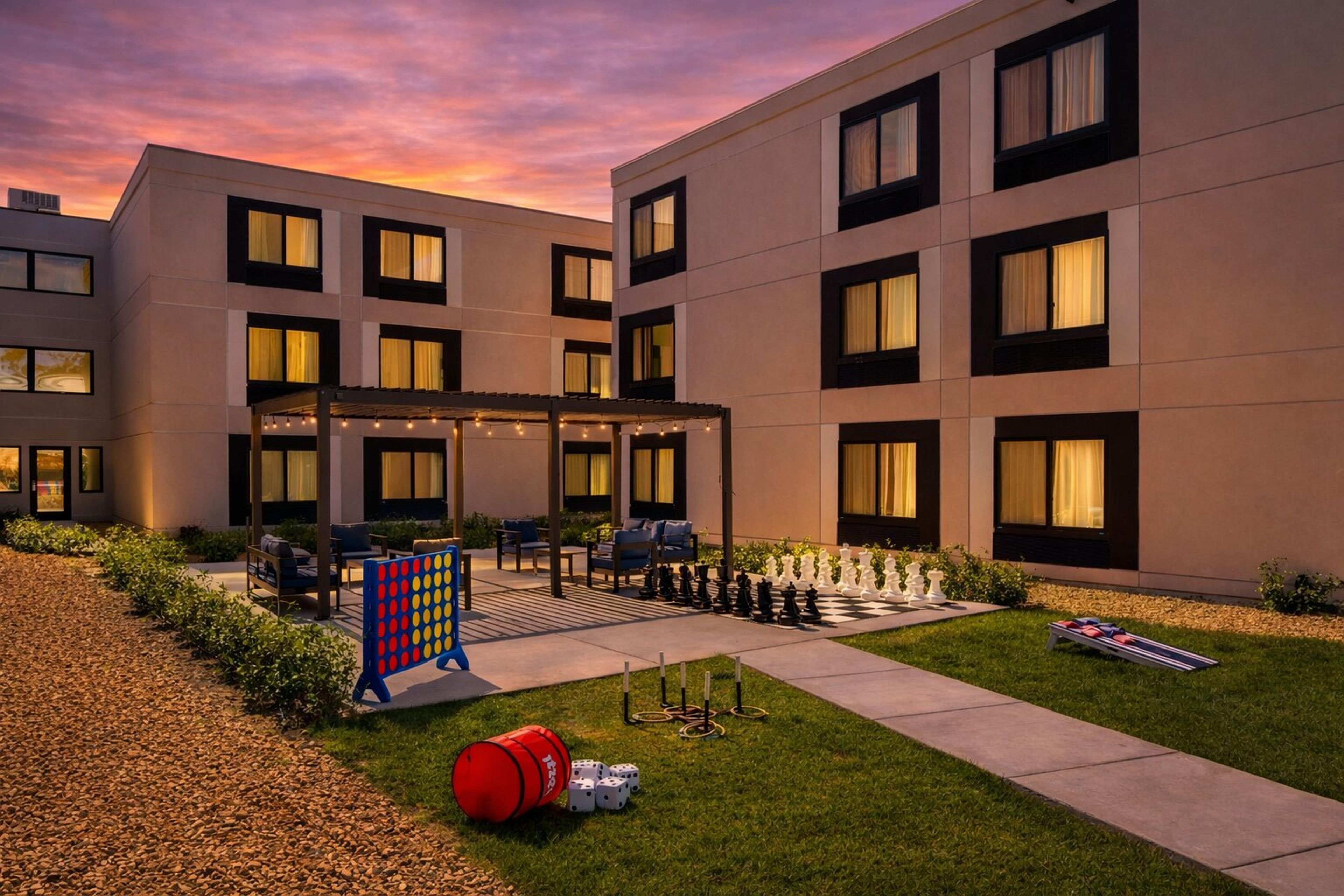 Un hotel moderno con un patio que ofrece mesas al aire libre, una mesa de ajedrez y un césped bien cuidado.