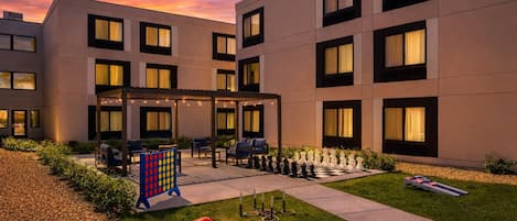 A modern hotel with a courtyard featuring outdoor seating, a chess table, and a well-maintained lawn.
