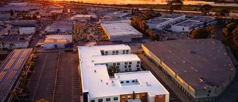 An aerial view of a commercial area with multiple buildings, parking lots, and a large body of water in the background.