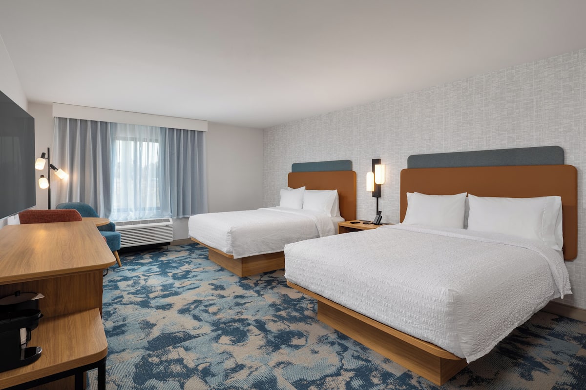 A hotel room with two beds, a desk, a chair, and a large window with curtains.