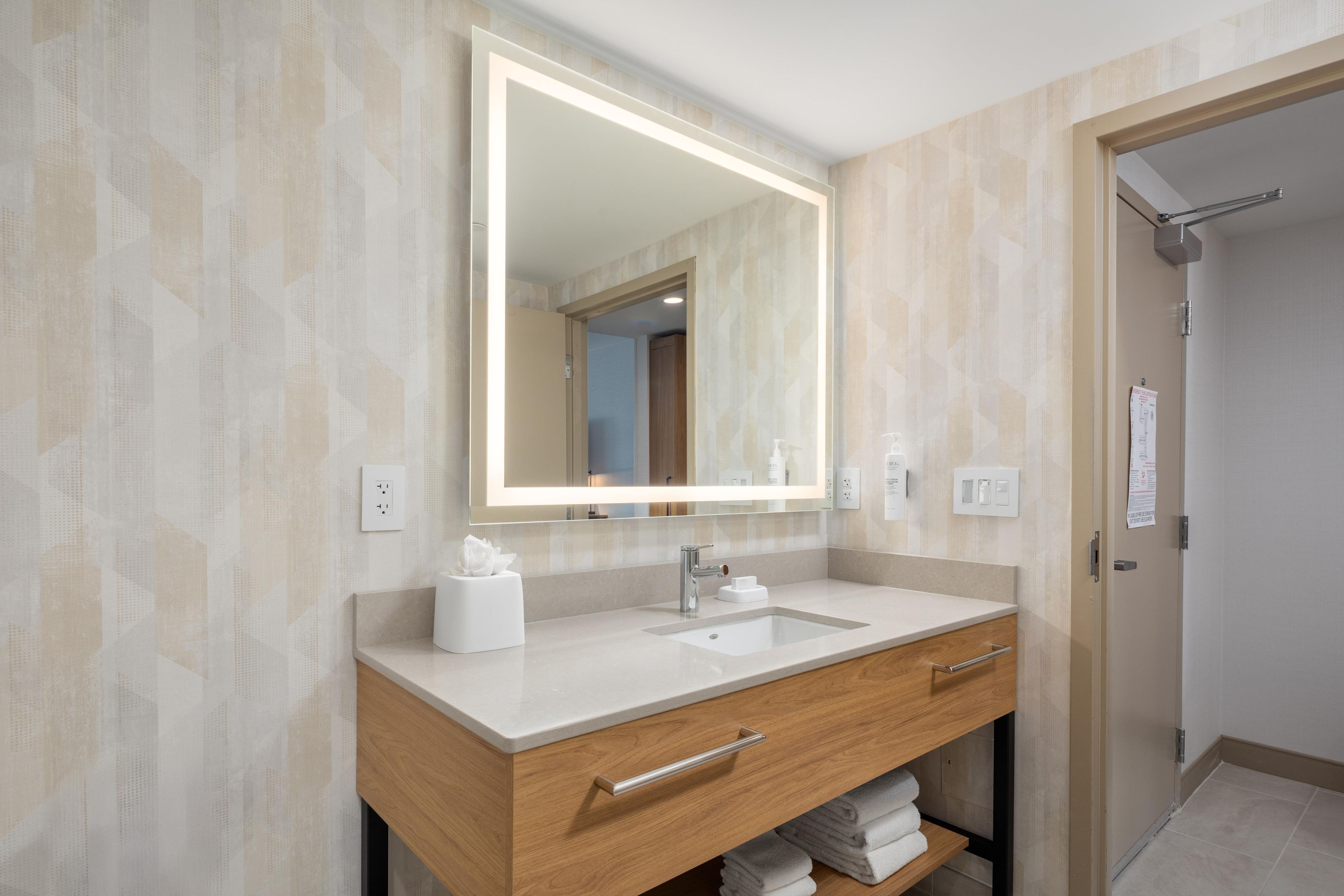 A modern bathroom with a large mirror, a sink, and a towel rack.