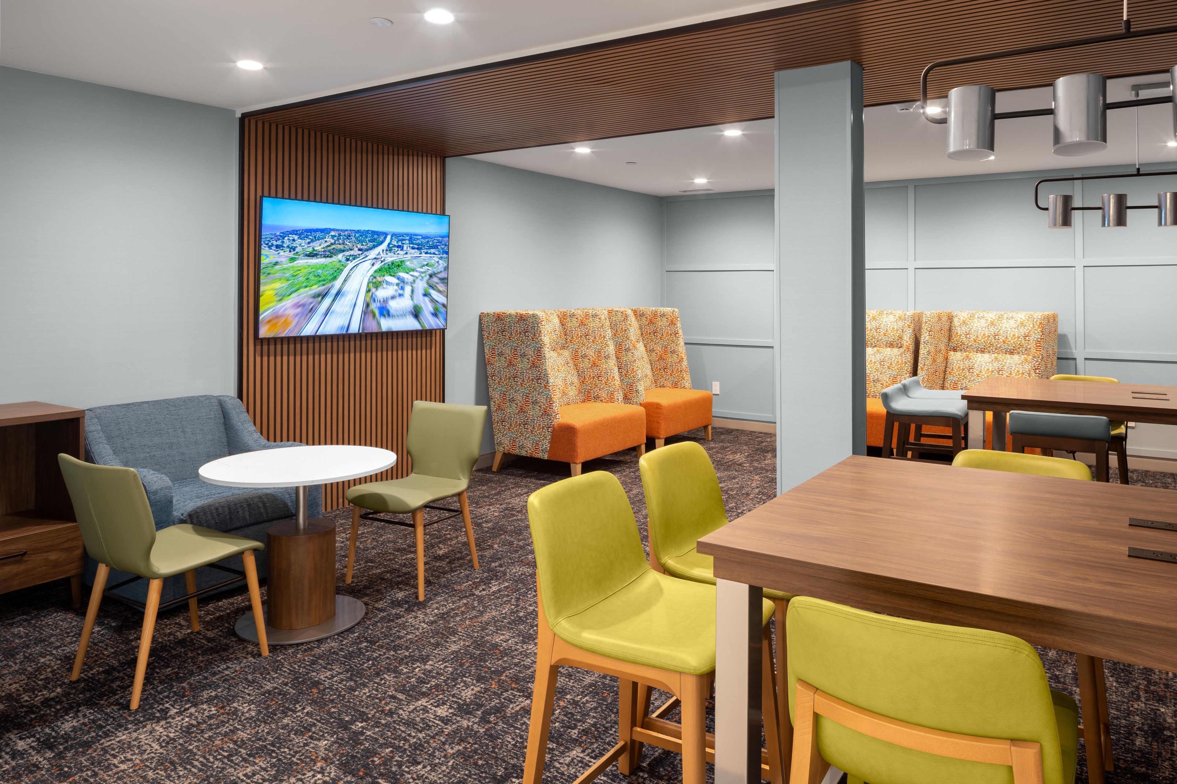 A modern hotel room with a large flat-screen TV, comfortable seating, and a dining area.