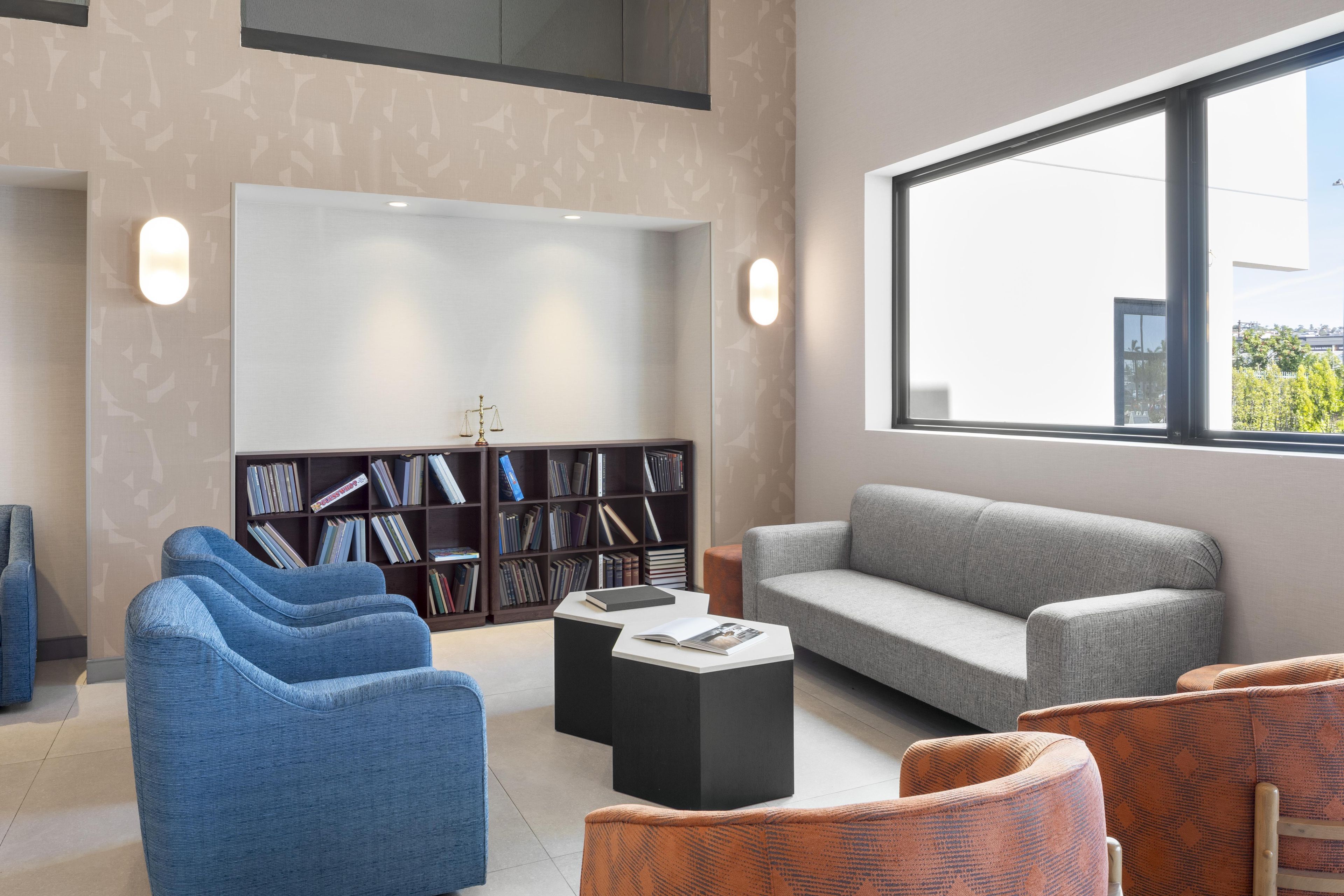 Ein modernes Wohnzimmer mit grauem Sofa, blauen Sesseln, einem schwarzen Couchtisch und einem Bücherregal.