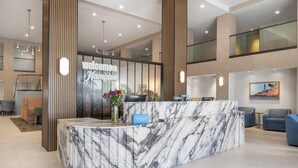 A modern hotel reception area with a marble counter, a 'Welcome to Hampton' sign, and a reception desk. - Hampton Inn & Suites by Hilton San Diego SeaWorld Near Old Town (San Diego)