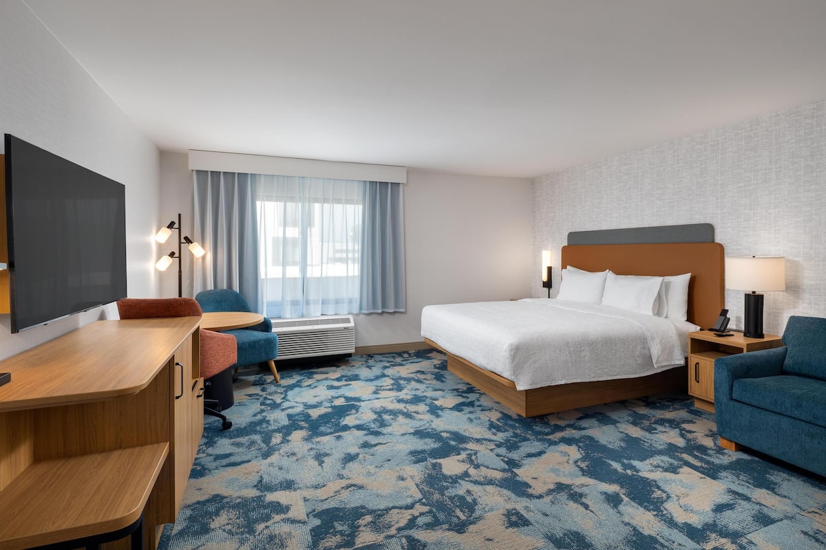 A hotel room with a bed, desk, chair, and a large window with curtains.