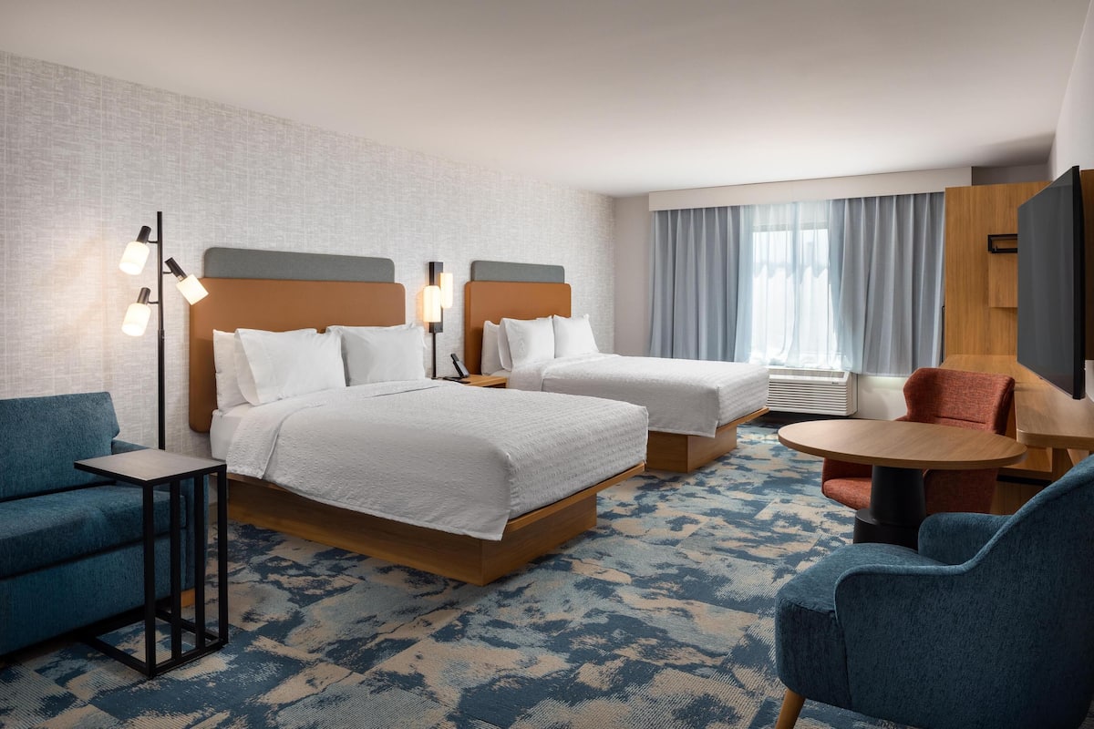 A hotel room with two beds, a sofa, a small table, and a TV.