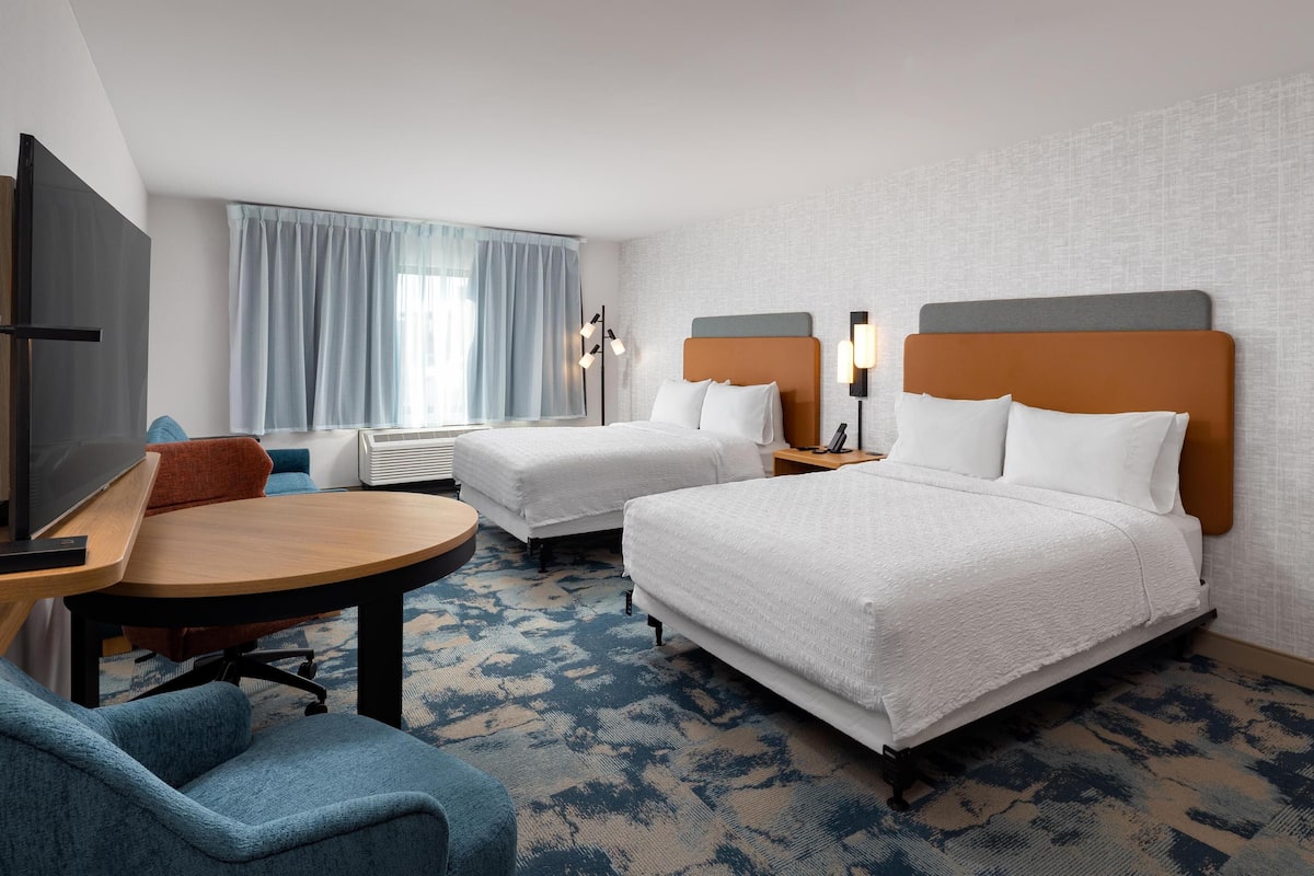 A hotel room with two beds, a desk with a chair, a TV, and a window with curtains.