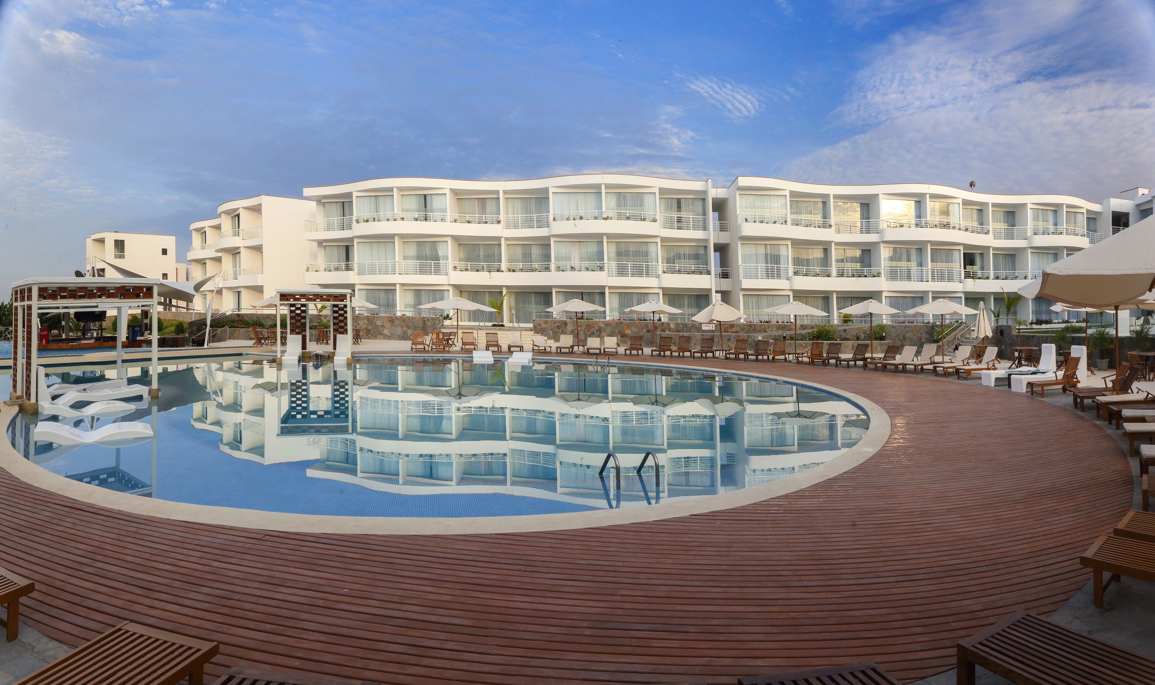 A hotel with a large pool, sun loungers, and a covered area with umbrellas.